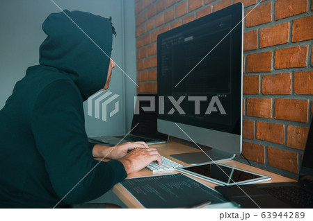 Hacker in the hood working with computer with 63944289