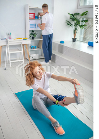 Female patient sitting on mat and stretching Female patient sitting on mat and stretching 63945729