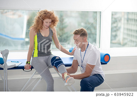 Male physiotherapist holding and examining leg of female patient, sitting on couch Male physiotherapist holding and examining leg of female patient, sitting on couch 63945922