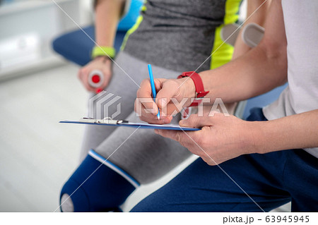 Male physiotherapist hands making notes, female patient sitting next to him Male physiotherapist hands making notes, female patient sitting next to him 63945945