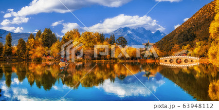 Panorama Landscape view of the Black Dragon Pool at Jade Spring Park with marble bridge over the Jade dragon mountain under blue sky, Lijiang, Yunnan province, China. China culture and travel concept Panorama Landscape view of the Black Dragon Pool at Jade Spring Park with marble bridge over the Jade dragon mountain under blue sky, Lijiang, Yunnan province, China. China culture and travel concept 63948112
