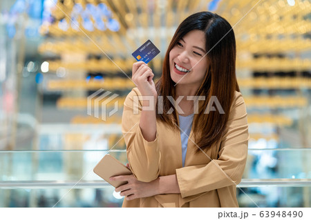 Portrait Asian woman holding and presenting the credit card for online shopping in department store over the clothes shop store background, technology money wallet and online payment concept Portrait Asian woman holding and presenting the credit card for online shopping in department store over the clothes shop store background, technology money wallet and online payment concept 63948490
