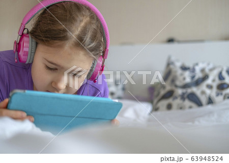 Girl in pink headphones with tablet device Girl in pink headphones with tablet device 63948524