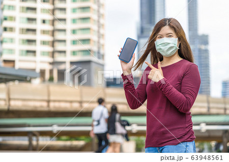 Asian woman hand showing smart mobile phone with safety medical face mask for prevent Coronavirus or Covid19 Outbreak when travel to work in business downtown, Health care and infection concept 63948561