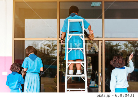 Back view of female students are helping to wipe the glass with wet newspaper at school. 63950431
