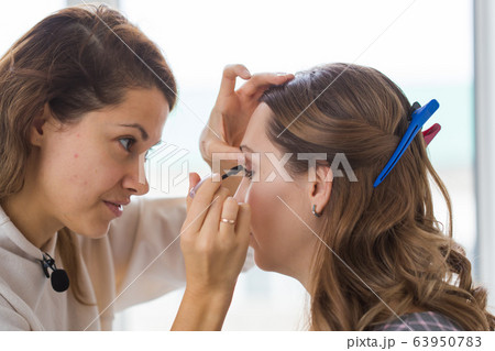 Beauty and cosmetics concept - Makeup artist doing professional make up of young woman Beauty and cosmetics concept - Makeup artist doing professional make up of young woman 63950783