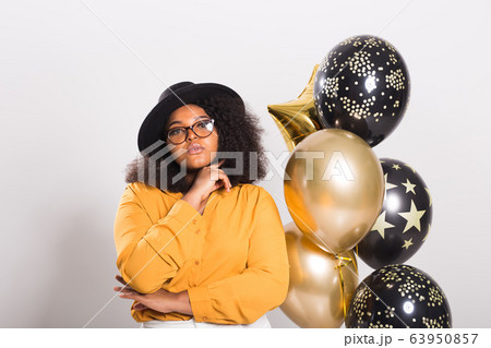 Holidays, birthday party and fun concept - Portrait of smiling young African-American young woman looking stylish on white background holding balloons. 63950857
