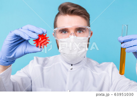 Covid-19, Vaccine development and medicine concept - Man scientist in flu mask and protective gloves holding a model of coronavirus and test tube. 63951030