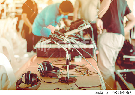 Two microphones with blue and red sponges placed on a stand with earphones on the table with blur image of the audio technician was installing and testing the sound system in the background. Two microphones with blue and red sponges placed on a stand with earphones on the table with blur image of the audio technician was installing and testing the sound system in the background. 63964062