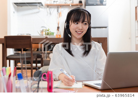 自宅でイヤホンをつけながらパソコンで話をする若い女性 63965814