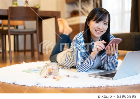 リビングで横になりながら、スマホを見る若い女性 リビングで横になりながら、スマホを見る若い女性 63965898