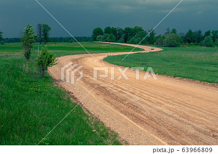 Yellow gravel road winding in a green field 63966809