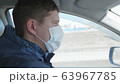 Guy is driving a car. The medical mask on the face. People use extra protection against coronavirus. 63967785