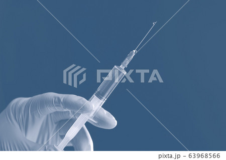 Doctor's white-gloved hand holding a syringe with transparent liquid isolated on a blue background. Doctor's white-gloved hand holding a syringe with transparent liquid isolated on a blue background. 63968566