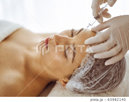 Beautician doing beauty procedure with syringe to face of young brunette woman. Cosmetic medicine and surgery, beauty injections Beautician doing beauty procedure with syringe to face of young brunette woman. Cosmetic medicine and surgery, beauty injections 63982140