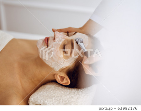 Beautiful brunette woman enjoying applying cosmetic mask with closed eyes. Relaxing treatment in medicine and spa center concepts Beautiful brunette woman enjoying applying cosmetic mask with closed eyes. Relaxing treatment in medicine and spa center concepts 63982176