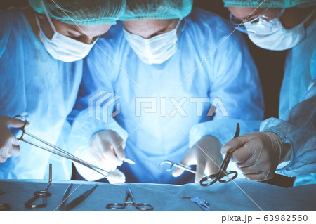 Group of surgeons wearing safety masks performing operation. Close-up of surgery tools. Medicine concept 63982560