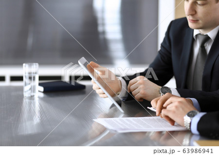 Businessman using tablet computer and work together with his colleague or partner at the glass desk in modern office, close-up. Unknown business people at meeting. Teamwork and partnership concept Businessman using tablet computer and work together with his colleague or partner at the glass desk in modern office, close-up. Unknown business people at meeting. Teamwork and partnership concept 63986941