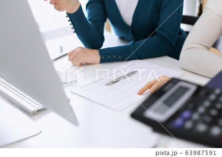 Accountant checking financial statement or counting by calculator income for tax form, hands closeup. Business woman sitting and working with colleague at the desk in office. Tax and Audit concept 63987591