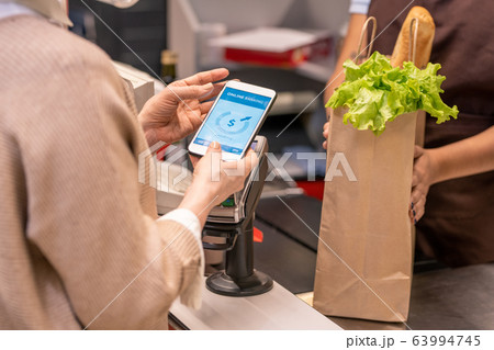 Hands of mature female buyer with smartphone over payment machine Hands of mature female buyer with smartphone over payment machine 63994745