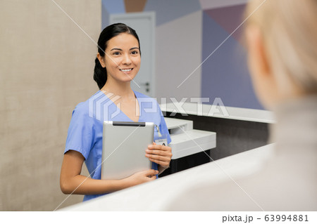 Cheerful young assistant or receptionist in blue uniform looking at patient 63994881