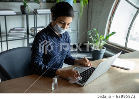 Young businesswoman in facial mask sanitizing laptop keyboard. 63995972