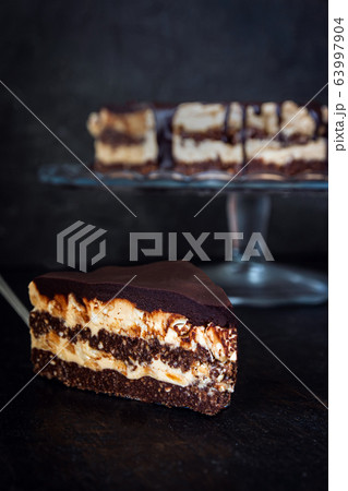 Slice and chocolate cake layers with butter-cream-nut cream with chocolate drips on a glass stand on 63997904