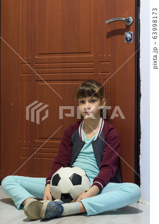 A girl with a ball sits at the door and is sad A girl with a ball sits at the door and is sad 63998173