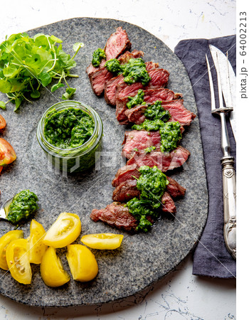 Slices of beef steak with chimmichuri sauce on gray stone plate 64002213