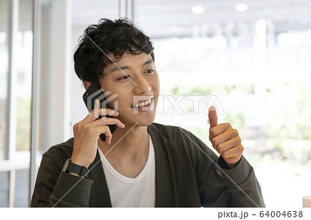 スマホで話しながら親指をたてる若い男性 スマホで話しながら親指をたてる若い男性 64004638