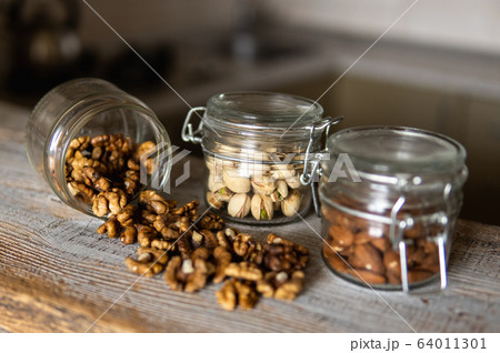 Walnut scattered on the white vintage table from a jar. Walnut is a healthy vegetarian protein nutritious food. Walnut kernels and whole walnuts on rustic old wood. 64011301