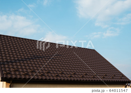 Brown metal tile roof. Roof metal sheets. Modern types of roofing materials. Roof of the house, metal roof tile against the blue sky. Building. Brown metal tile roof. Roof metal sheets. Modern types of roofing materials. Roof of the house, metal roof tile against the blue sky. Building. 64011547