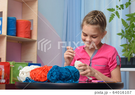 Girl knits a soft toy sitting at a table in the Girl knits a soft toy sitting at a table in the 64016107