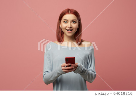 Happy girl with phone in her hands standing in studio 64019216