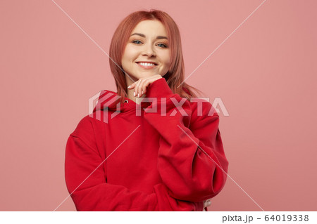 Smiling girl in red sweatshirt isolated empty pink background in studio 64019338