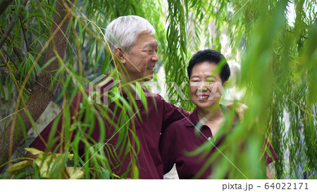 Happy retired Asian senior couple laughing under green willow tree background 64022171
