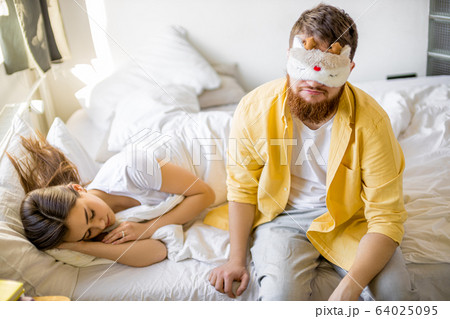 sleepy man in mask sit on bed near sleeping wife 64025095