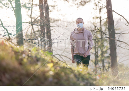 Corona virus, or Covid-19, is spreading all over the world. Portrait of caucasian sporty woman wearing a medical protection face mask while walking in the forest. Corona virus. 64025725