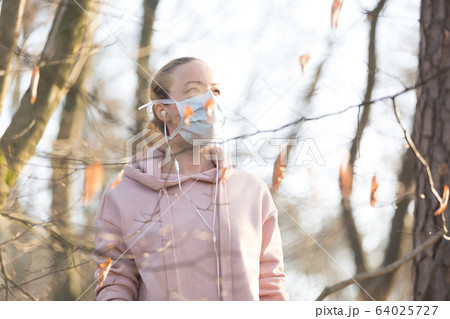 Portrait of caucasian sporty woman wearing medical protection face mask while walking in park, relaxing and listening to music. Corona virus, or Covid-19, is spreading all over the world 64025727