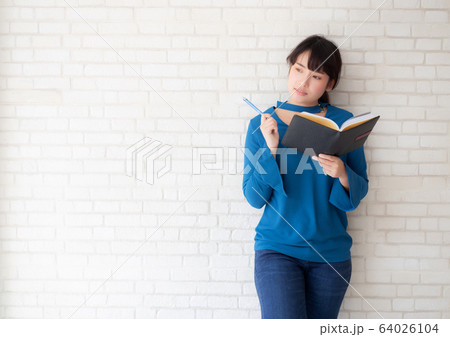Beautiful asian woman smiling standing thinking and writing notebook on concrete cement 64026104
