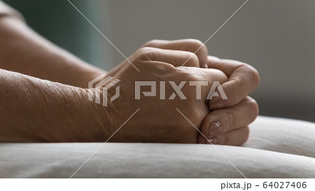 Side view close up wrinkled clasped hands on lap. 64027406