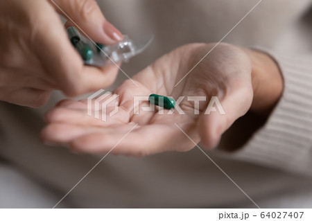 Middle aged woman pouring capsules pills out of plastic blister. Middle aged woman pouring capsules pills out of plastic blister. 64027407