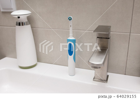 An electric toothbrush and an old toothbrush near the washbasin. An electric toothbrush and an old toothbrush near the washbasin. 64029155