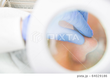 Beautician examines pores with magnifying mirror 64029186