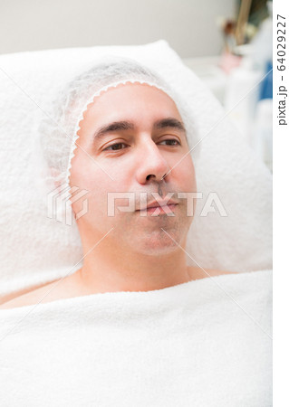 Man face and head in disposable cap in spa salon Man face and head in disposable cap in spa salon 64029227