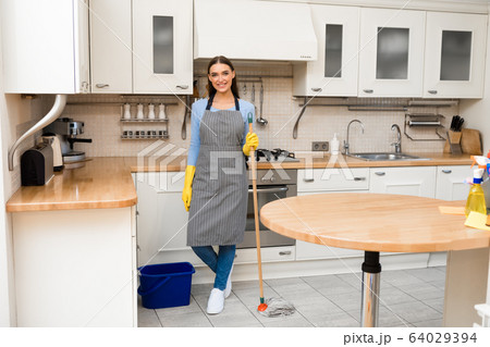 Young woman holding mop standing in kitchen Young woman holding mop standing in kitchen 64029394