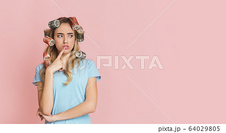 Pensive housewife presses finger to her lips 64029805
