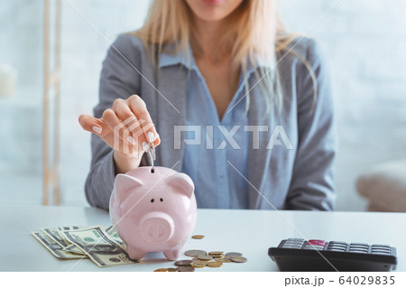 Girl puts coin piggy bank, near cash and calculator Girl puts coin piggy bank, near cash and calculator 64029835