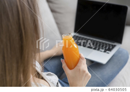 Unrecognizable woman working on laptop and drinking detox orange juice Unrecognizable woman working on laptop and drinking detox orange juice 64030505