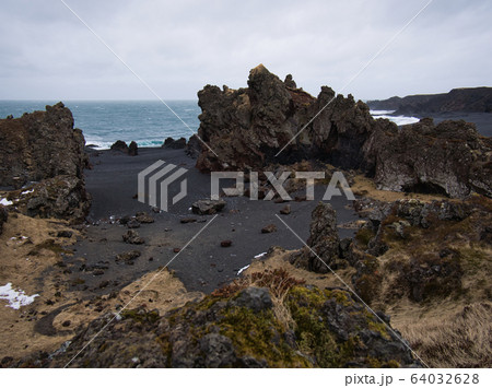 Rugged lava rocks on a black sandy beach Rugged lava rocks on a black sandy beach 64032628